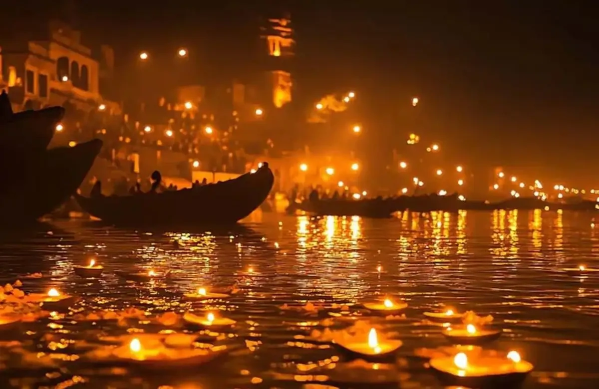 A boat moving past diya-lit ghats at dusk
