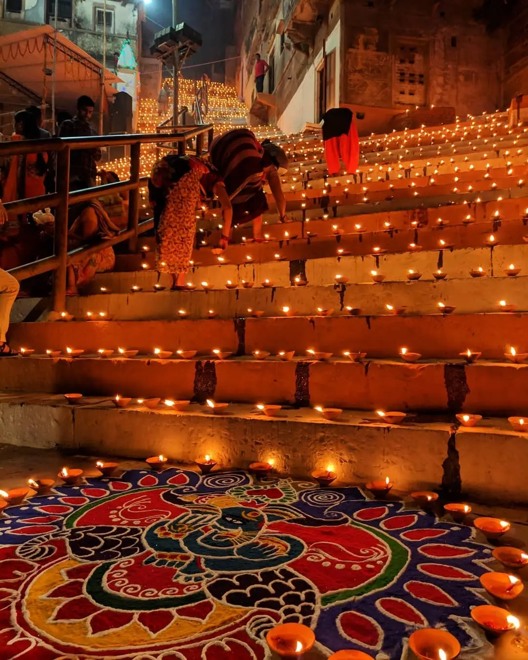 Colourful rangoli patterns and rows of glowing diyas decorating the ghat steps